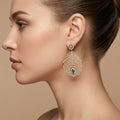 Boucles d'oreilles pendantes plumes de paon en or jaune 18k serties de pierres, pierres vertes - bijou porté par une mannequin