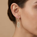 Boucles d'oreilles pendantes en or jaune 18k ovales sertis de pierres - bijou porté par une mannequin