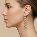 Boucles d'oreilles pendantes en or rose 18k pyramides pavées de pierres - bijou porté par une mannequin