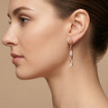 Boucles d'oreilles pendantes en or rose 18k branches serties de pierres - bijou porté par une mannequin