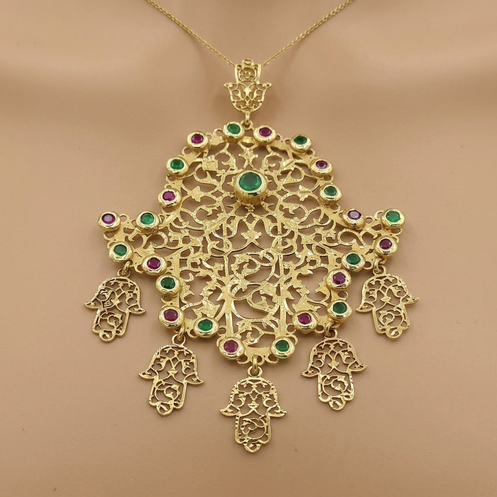 Pendentif khmissa ajourée en or jaune 18k serti de pierres vertes et rouges, pampilles mains de Fatma - bijou porté par une mannequin