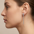 Boucles d'oreilles pendantes en or blanc 18k rangées de pierres serties - bijou porté par une mannequin